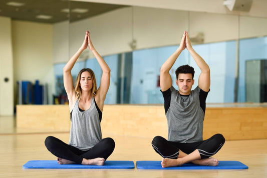 A man and woman practicing yoga poses together in a well-lit gym environment.