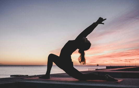 A woman practicing yoga poses against a vibrant sunset backdrop, with warm colors illuminating the serene scene.