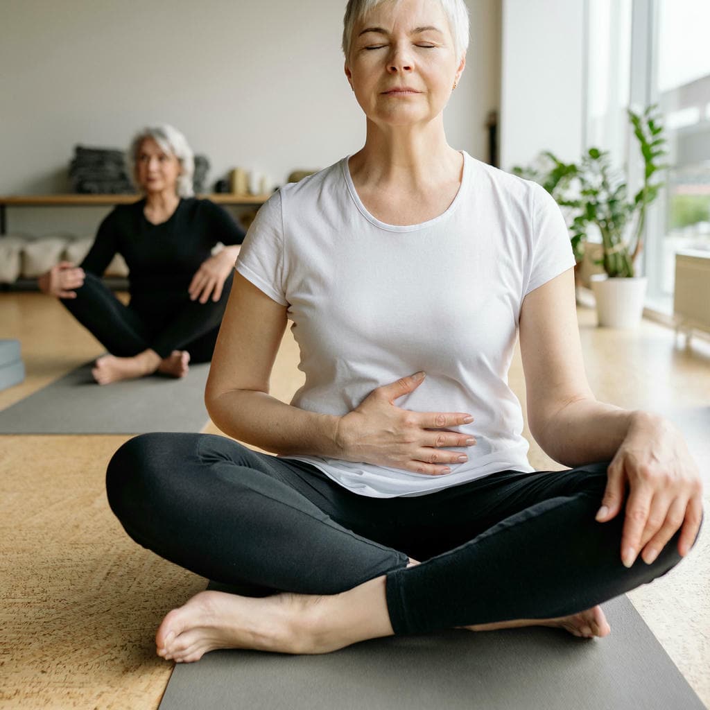 Person meditating in white shirt and black leggings, with another in background.